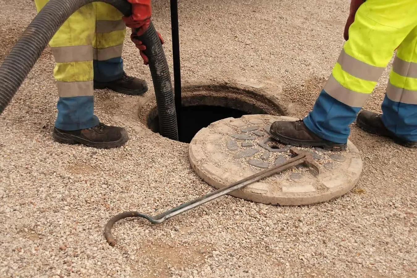 Drainage technicians clearing a manhole using a suction or jetting hose.