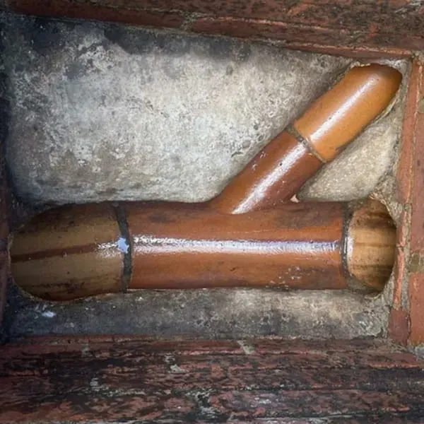 A close-up view of clay drain pipes forming a Y-junction inside a concrete inspection chamber, showing the drainage infrastructure.