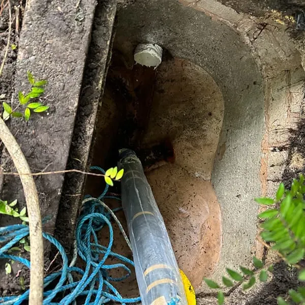High-pressure water jetting hose clearing a blocked drain in an open outdoor manhole.