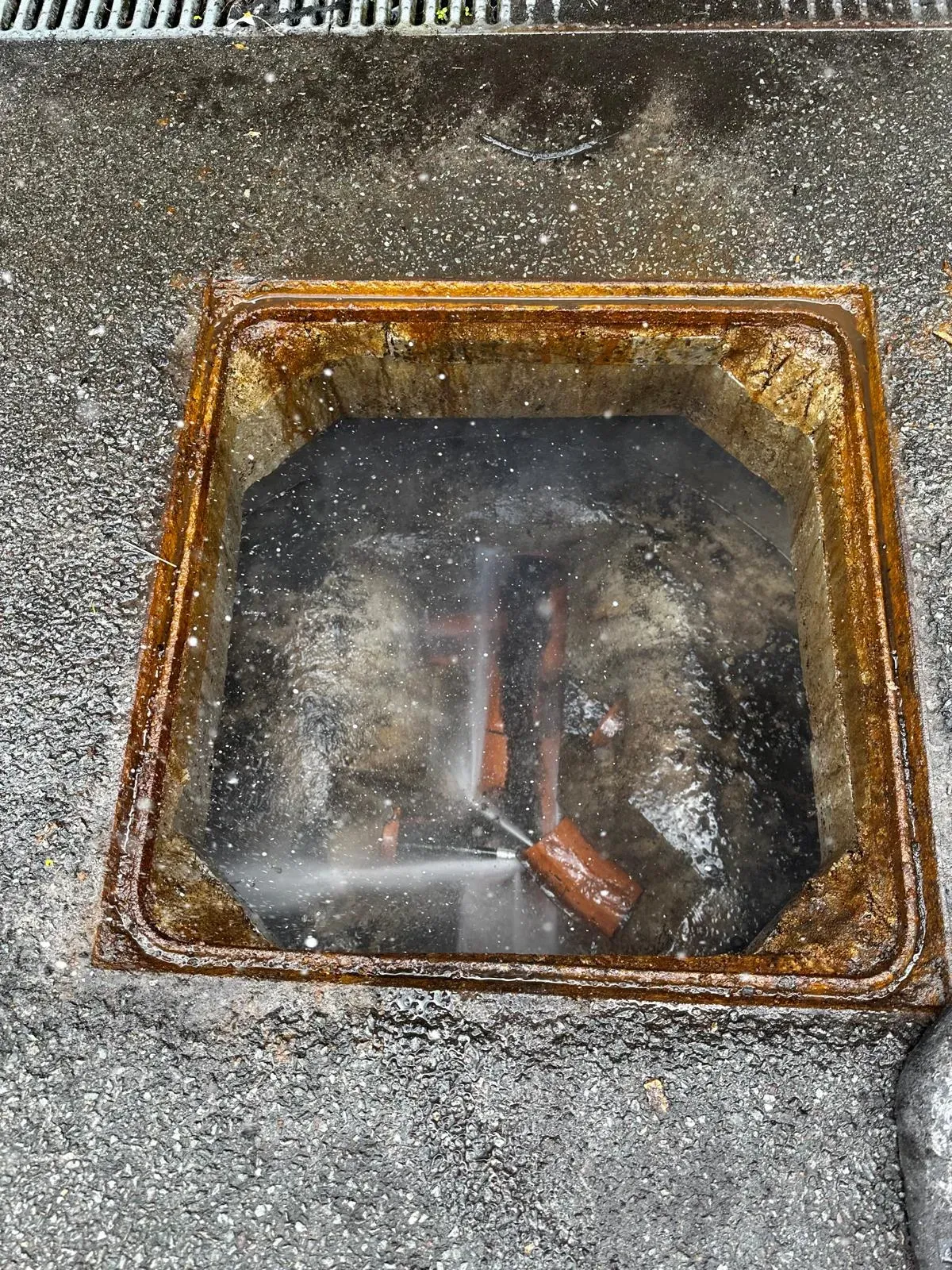 A professional using high-pressure water jetting to unblock an outdoor drain.